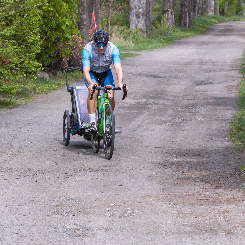 Ein Radfahrer mit Anhänger fährt einen schmalen, von Bäumen gesäumten Weg entlang.