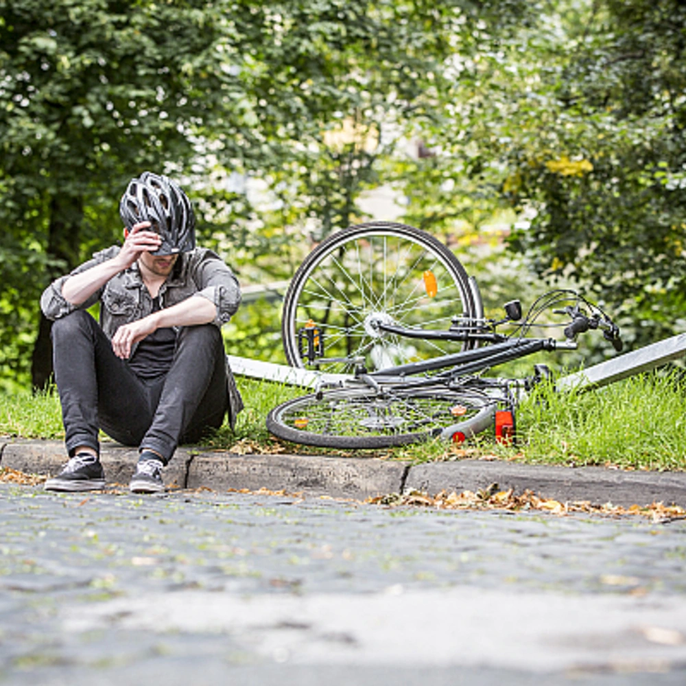 Radfahrer sitzt am Wegrand nach einem Sturz mit kaputtem Fahrrad