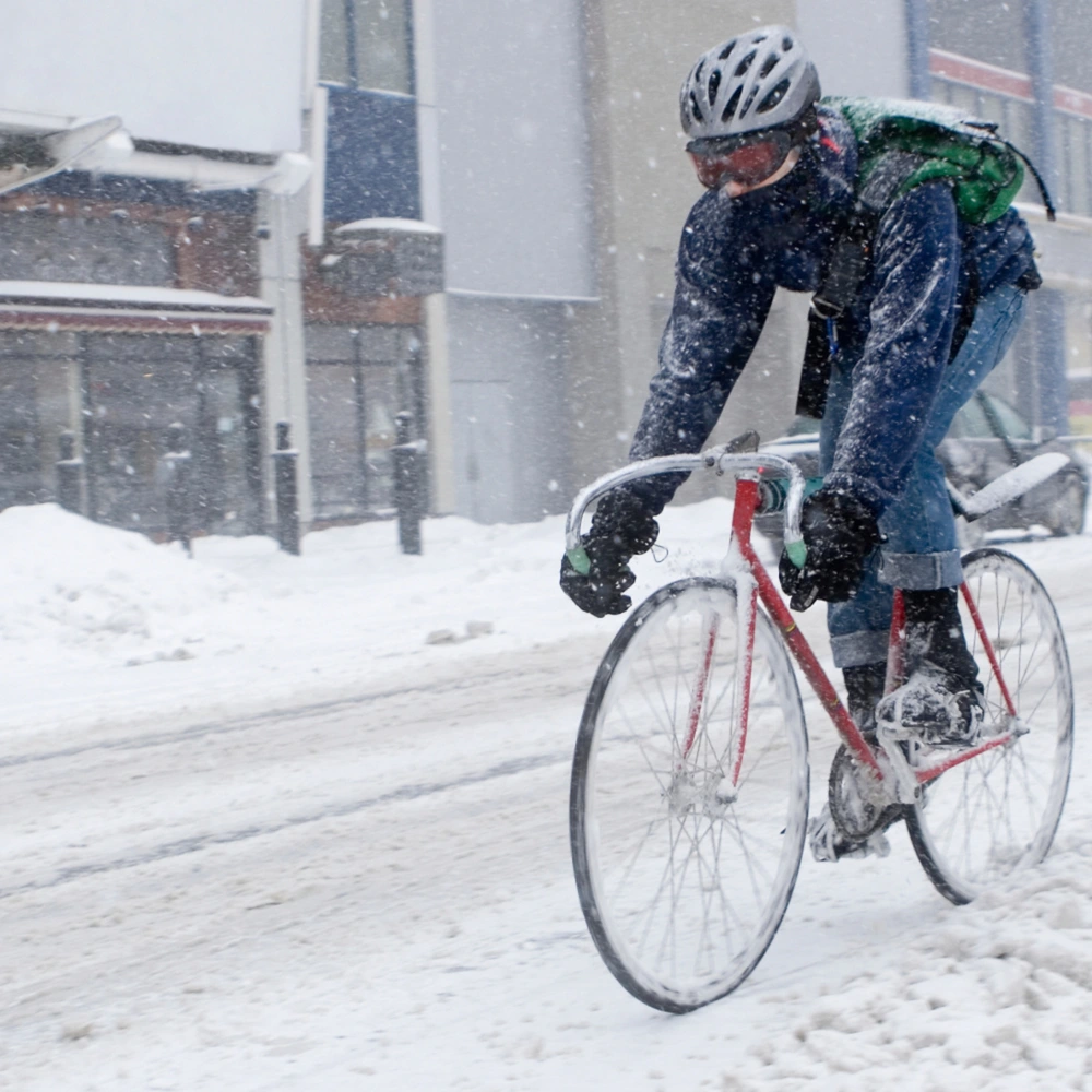 Radfahrer kämpft bei starkem Schneefall auf einer verschneiten Straße.