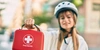 Reiseapotheke für Fahrradfahrende Frau hält eine Reiseapotheke in der Hand und trägt einen Fahrradhelm