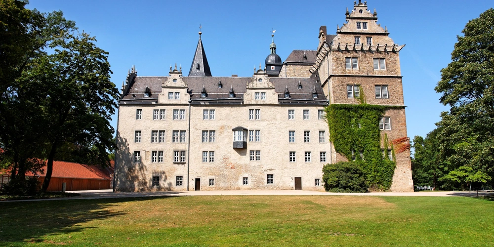 Historisches Schloss mit Türmen und grünem Garten unter klarem Himmel.