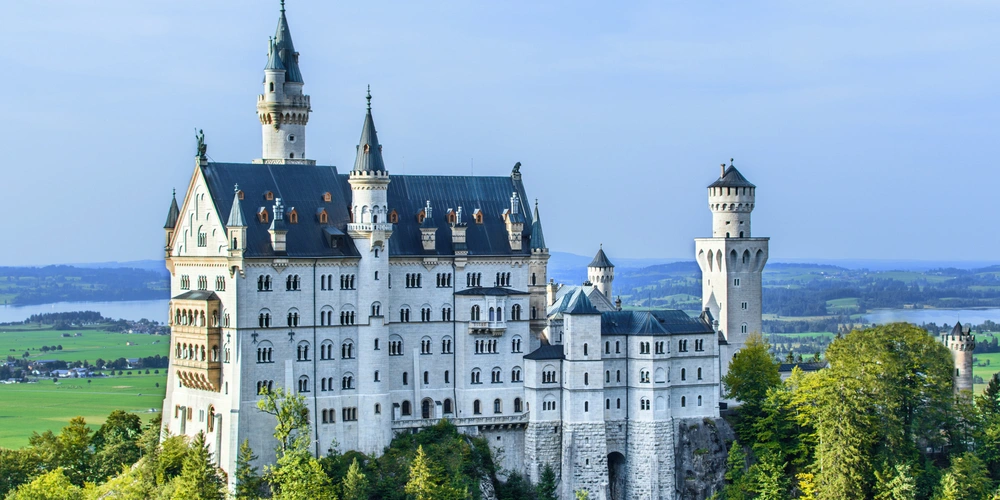 Neuschwanstein Schloss mit mittelalterlicher Architektur, umgeben von grünen Wäldern und blauem Himmel.