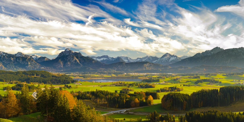 Blick auf eine lebendige Almlandschaft mit Bergen und bunten Bäumen unter einem blauen Himmel.