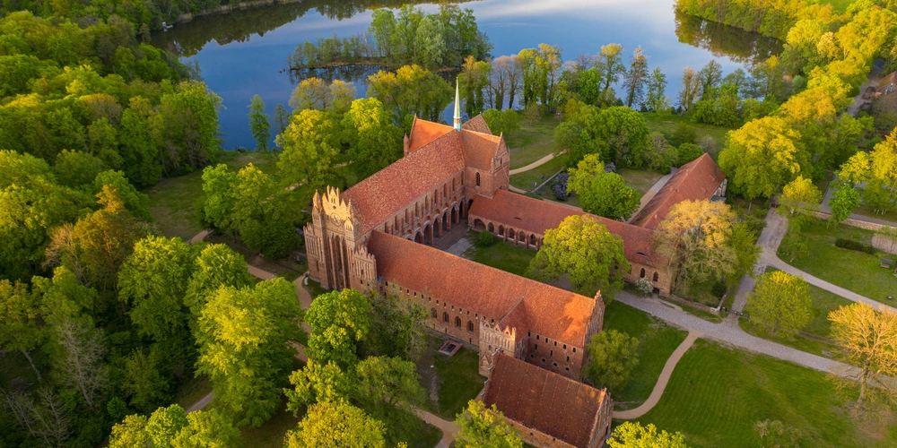 Aussicht auf ein historisches Gebäude umgeben von grünen Bäumen und einem blauem See.