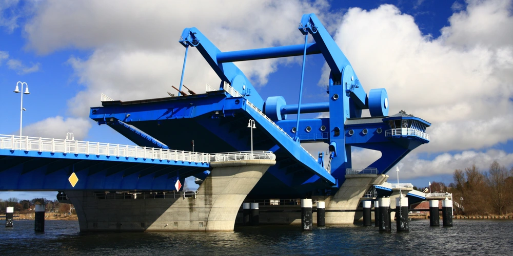 Blaues Brückenbauwerk mit angehobenem Brückenteil über Wasser unter bewölktem Himmel.