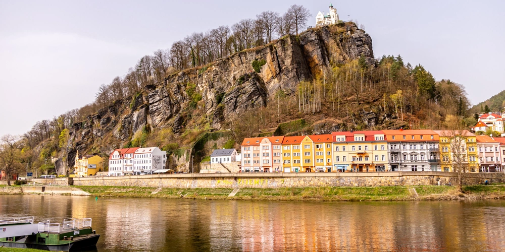 Felsige Landschaft mit Häusern am Fluss und im Hintergrund eine Burg.