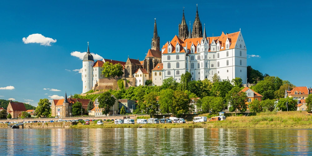 Eine malerische Landschaft mit einem Schloss auf einem Hügel, umgeben von Bäumen und Wasser.