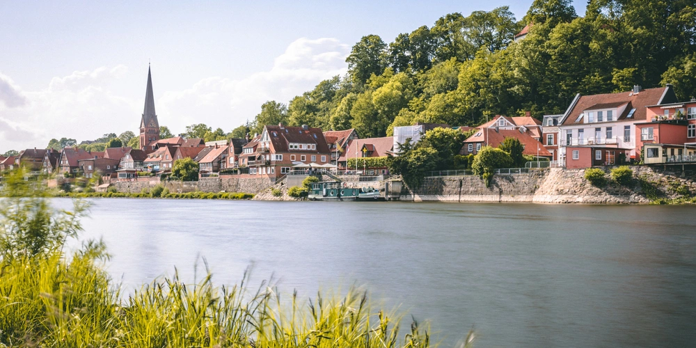 Blick auf eine malerische Stadt am Fluss mit historischen Häusern und einem Kirchturm.