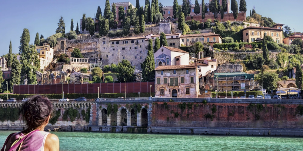 Frau steht an der Etsch, die durch Verona fließt und blickt auf das Stadtpanorama