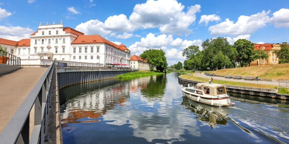 Blick auf ein verlassenes Schloss am Fluss, Boot fährt vorbei, blauer Himmel mit Wolken.