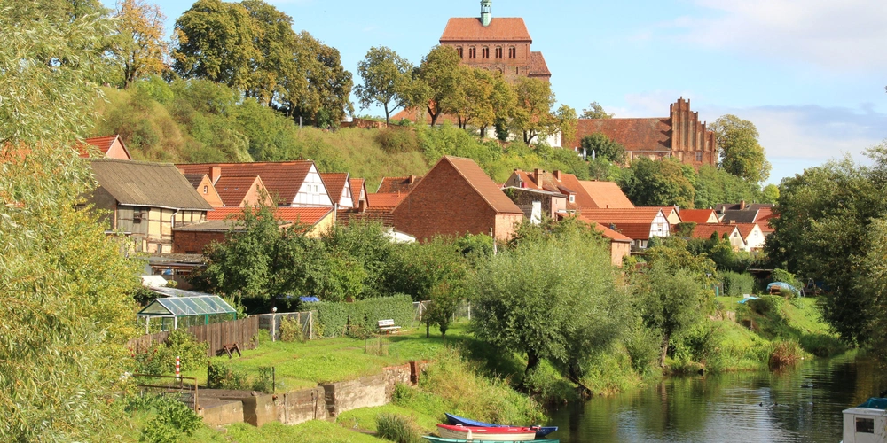 Idyllische Uferlandschaft mit historischen Gebäuden und grünen Bäumen.