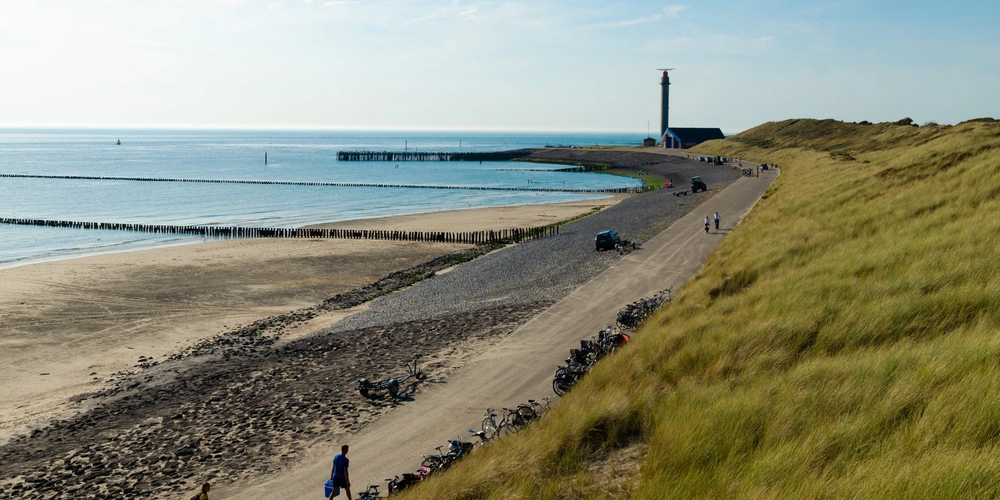 Küstenlandschaft mit Sandstrand, Dünen und einem Leuchtturm im Hintergrund.