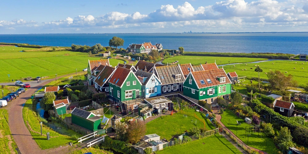 Farbenfrohe Häuser in einer ländlichen Landschaft am Meer, umgeben von Wiesen und Himmel.