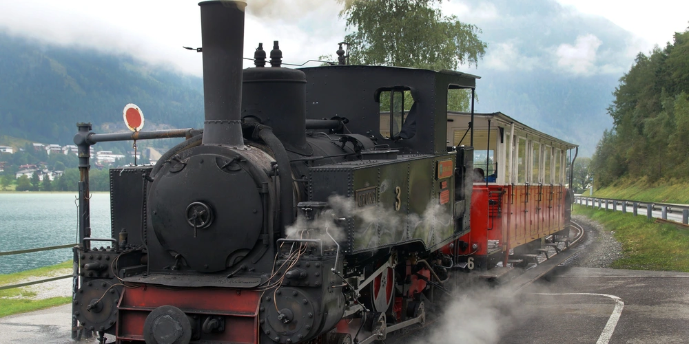 Dampflok mit historischen Waggons fährt an einem See entlang