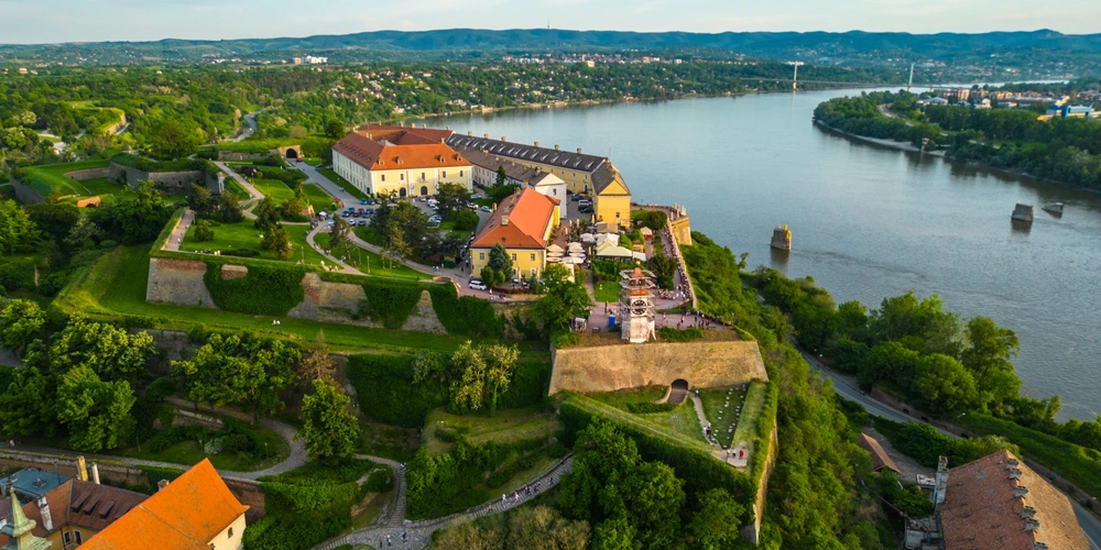 Luftaufnahme einer malerischen Festung am Fluss mit grünen Hügeln und Häusern.