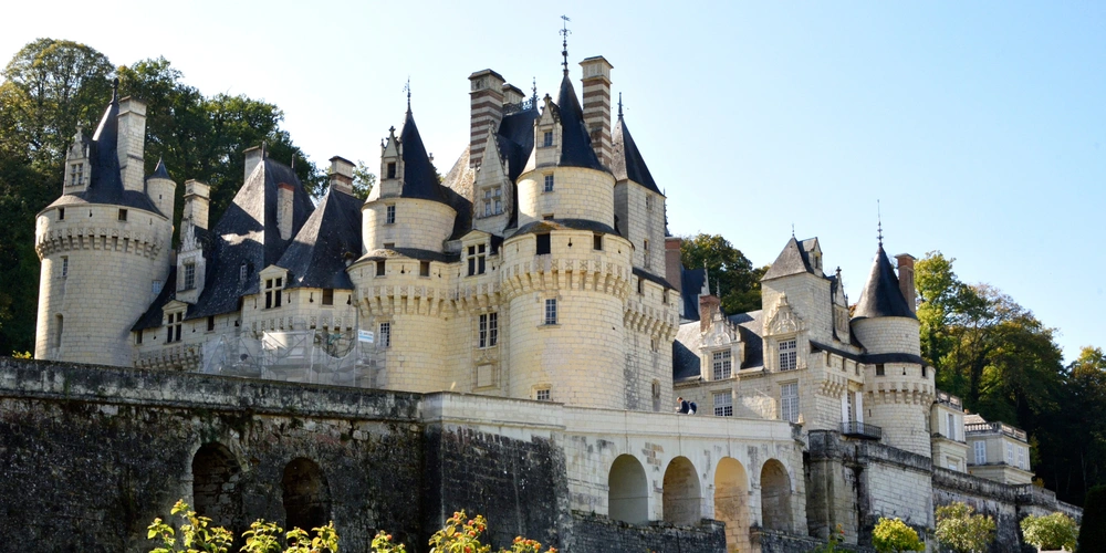 Ein malerisches Schloss mit vielen Türmen und Zinnen, umgeben von Bäumen und blauem Himmel.