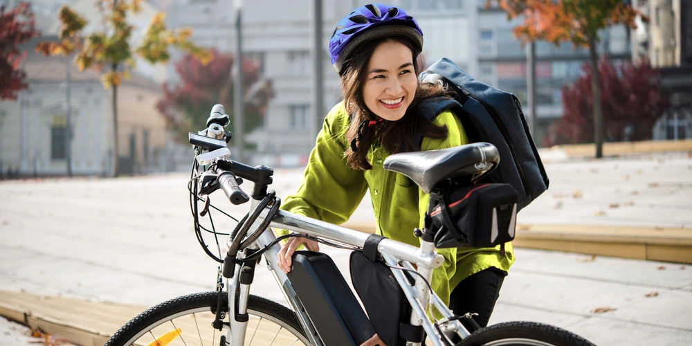 Radfahrerin setzt einen Akku in ihr E-Bike ein bei herbstlichen Ambiente