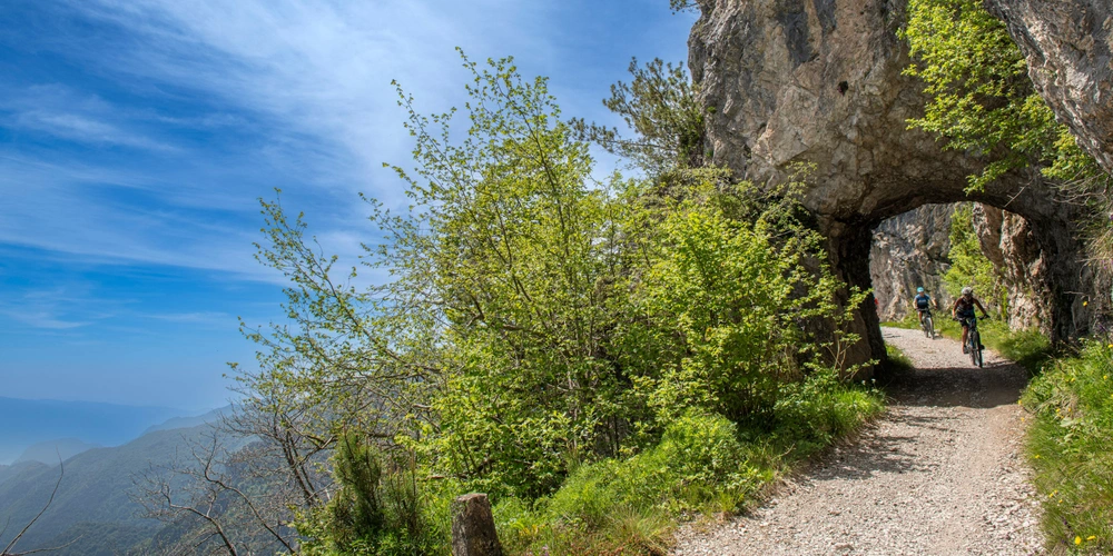 Wanderer auf einem schmalen Weg durch einen steinernen Tunnel, umgeben von Grün.