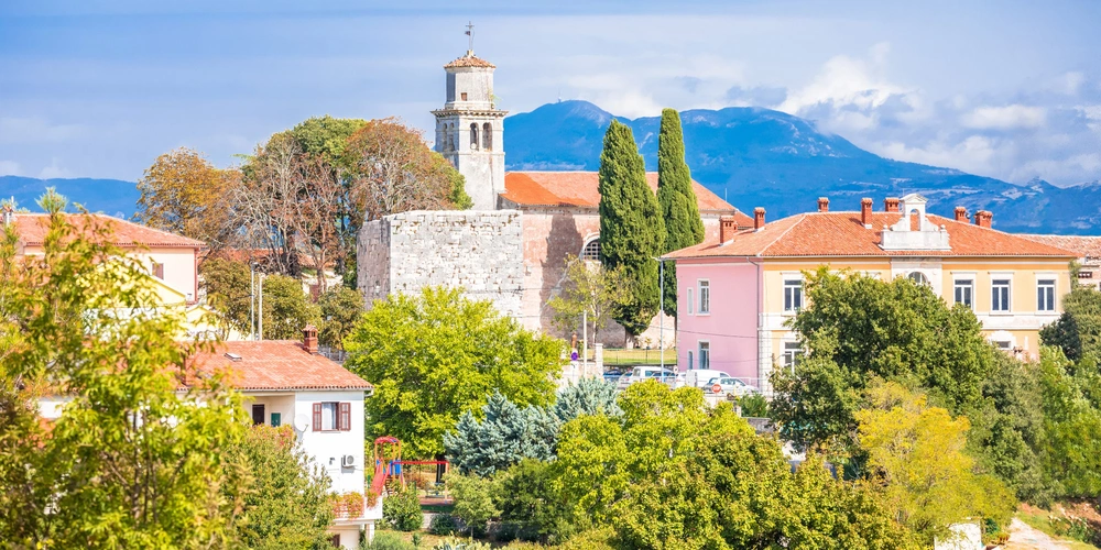 Charmante Landschaft mit historischen Gebäuden von Barban und einer Kirche, umgeben von Bäumen.