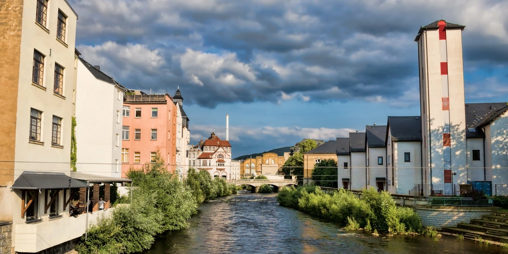 Aue an der Mulde Blick auf eine malerische Stadt mit bunten Häusern und einem Fluss unter bewölkten Himmel.