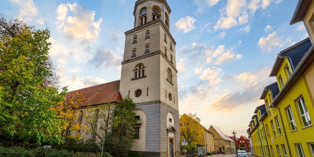Bad Düben Ein historischer Kirchturm zwischen bunten Häusern bei Sonnenuntergang.