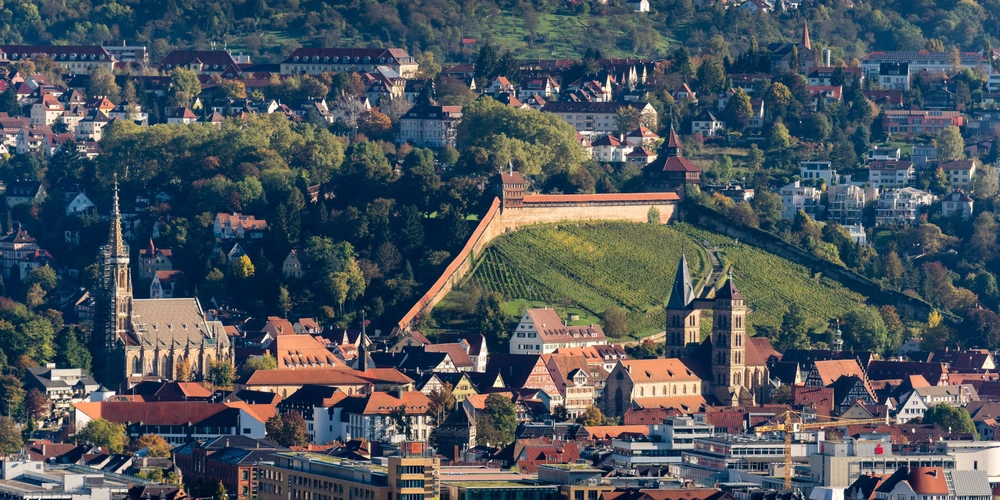 Blick auf die Stadt mit einer Stadtmauer und grünen Hügeln im Hintergrund.