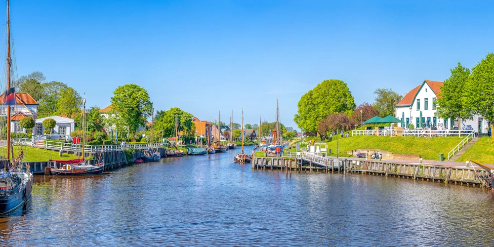 Blick auf einen ruhigen Hafen, Carolinensiel mit Booten und grünen Ufern unter blauem Himmel.