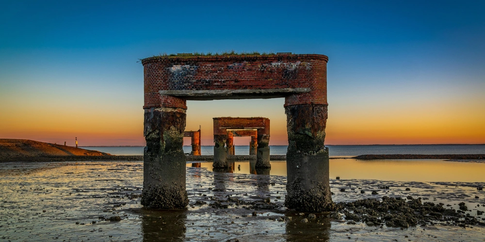 Verfallene Hafenstrukturen vor einem farbenfrohen Sonnenuntergang am Meer.