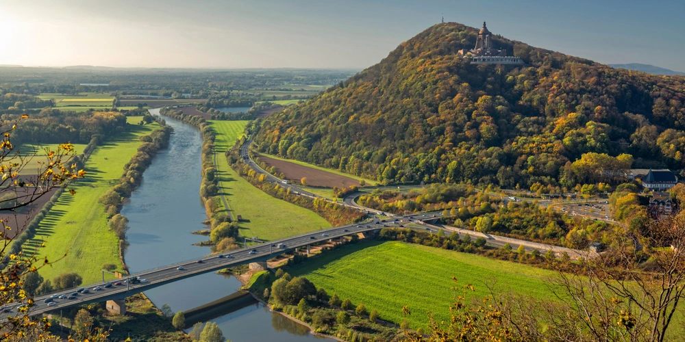 Panoramablick auf die Weser, Hügel und herbstlich gefärbte Landschaft.
