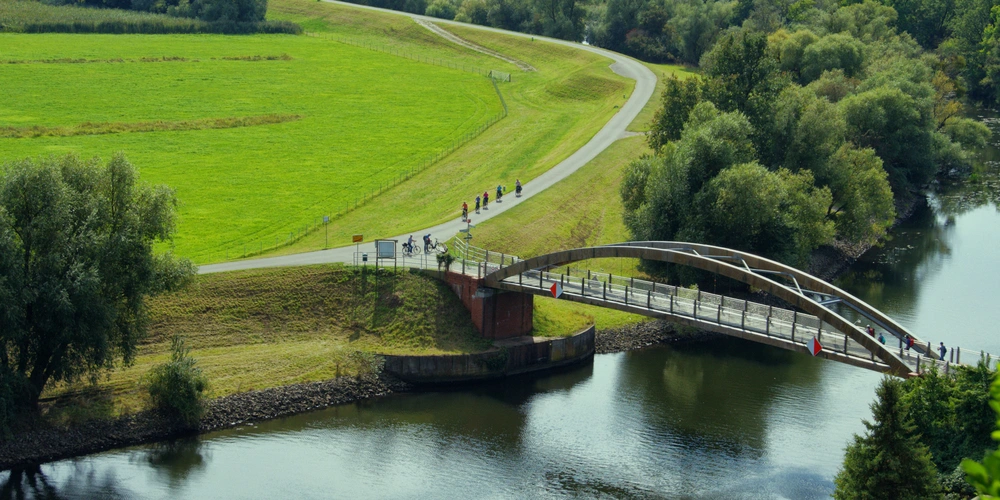 Eine Brücke über einen Fluss, umgeben von üppigem Grün und Spaziergängern.
