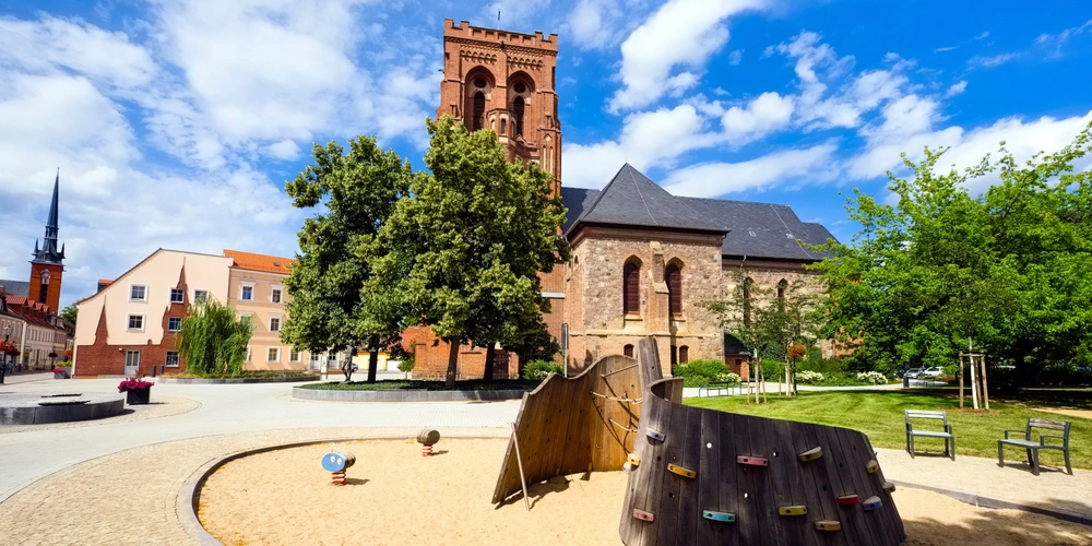 Historisches Kirchengebäude mit Blumen und Spielplatz unter blauem Himmel.