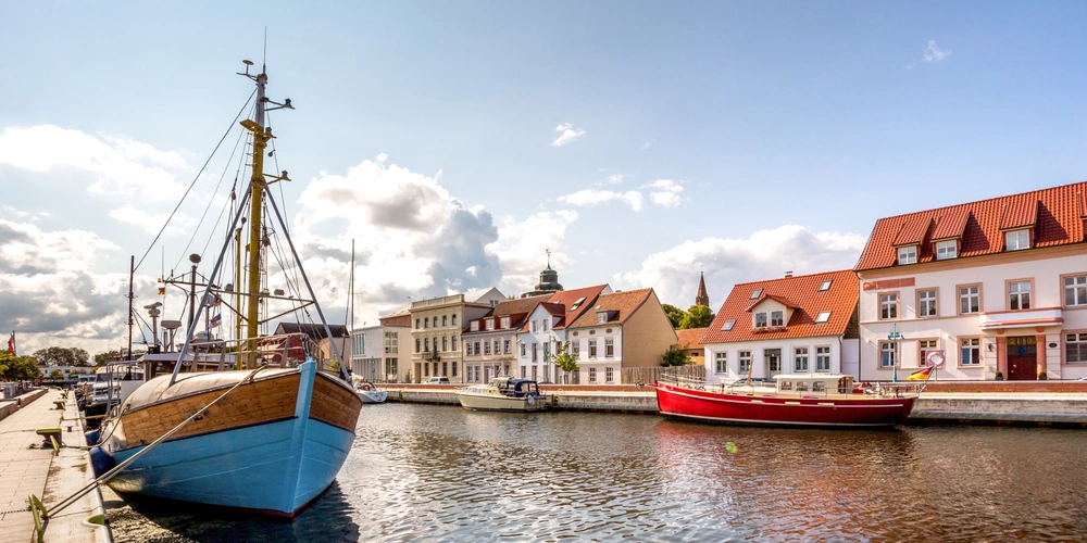 Der Hafen mit einem Holzboot und bunten Häusern unter einem blauen Himmel.