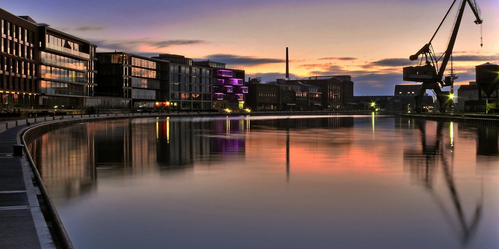 Stadtansicht mit einem ruhigen Gewässer und modernen Gebäuden während des Sonnenuntergangs.
