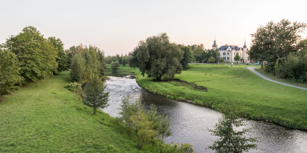 Die Zwicklauer Mulde: Idyllische Landschaft mit einem Fluss und einem Herrenhaus im Hintergrund