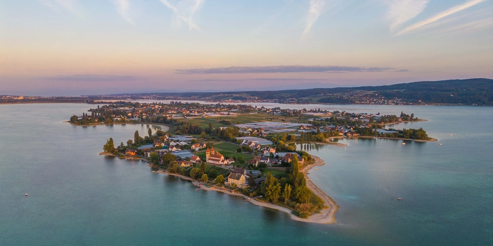 Luftaufnahme einer Insel mit Wohnungen, umgeben von ruhigem Wasser und einem farbenfrohen Himmel.