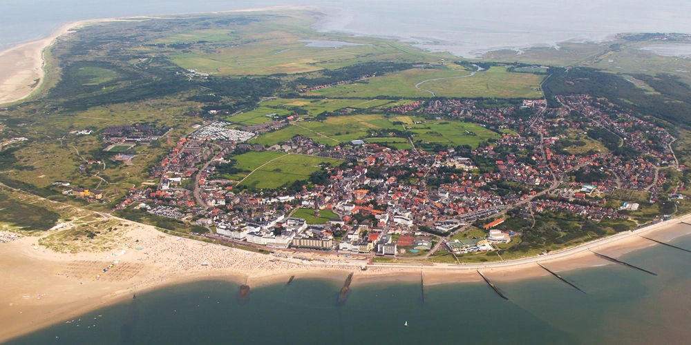 Luftaufnahme von der Nordseeinsel Borkum umgeben von Wasser, Strand und grünen Feldern.
