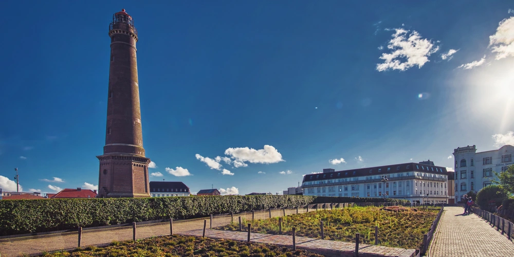Der große, graue Leuchtturm neben einer grünen Parklandschaft und blauem Himmel.