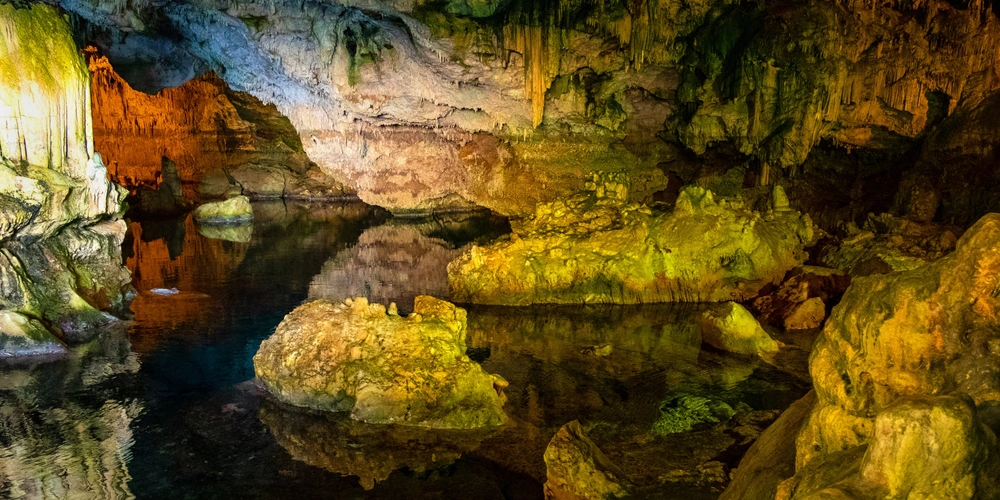 Bunte Stalaktiten und Wasser reflektieren in einer unterirdischen Höhle.
