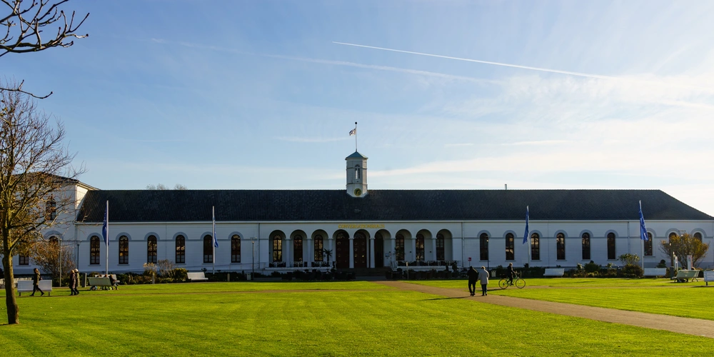 Historisches Gebäude mit Säulenfront, umgeben von grünem Rasen und Bäumen.