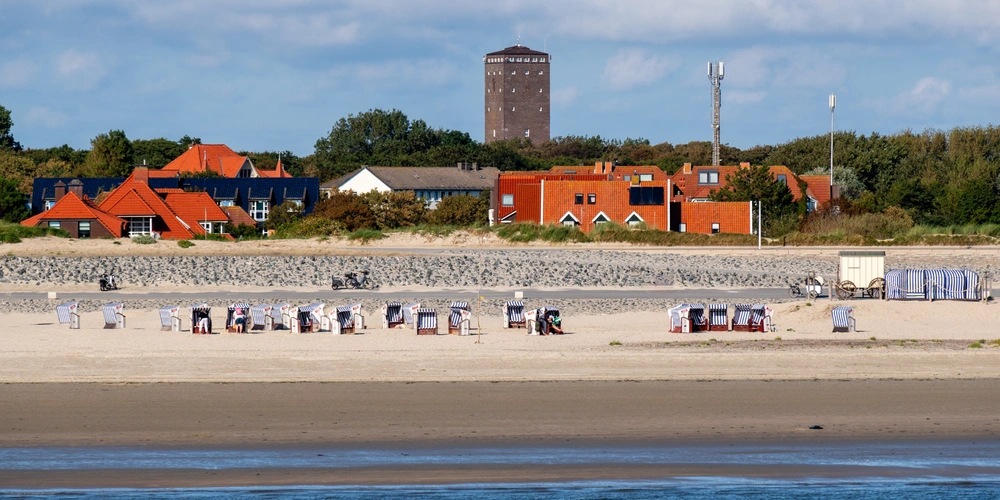 Strand mit Strandkörben, roten Häusern im Hintergrund und einem Wasserturm.