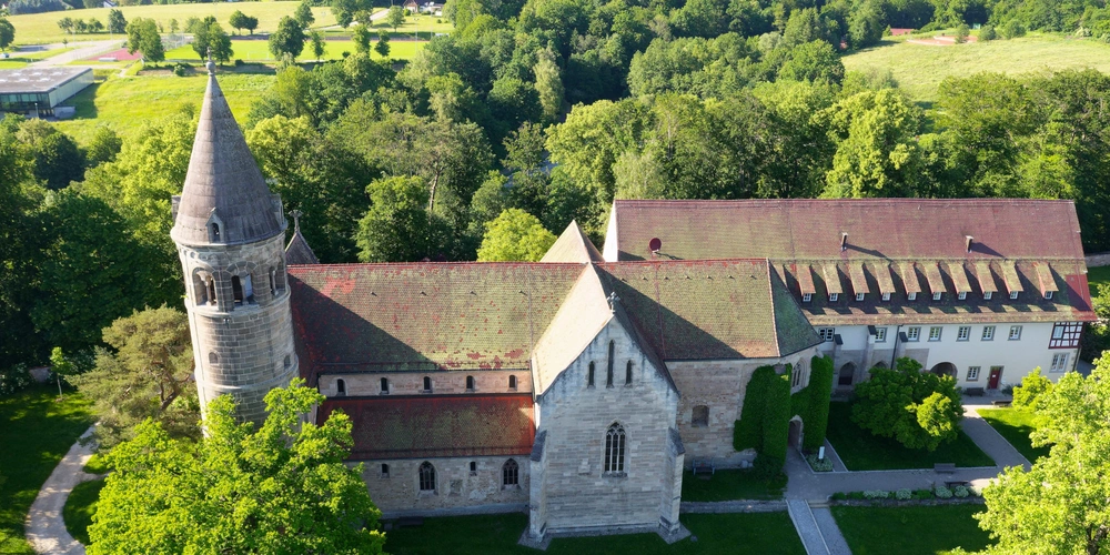 Historisches Gebäude mit Türmen, umgeben von grünen Wiesen und Bäumen.