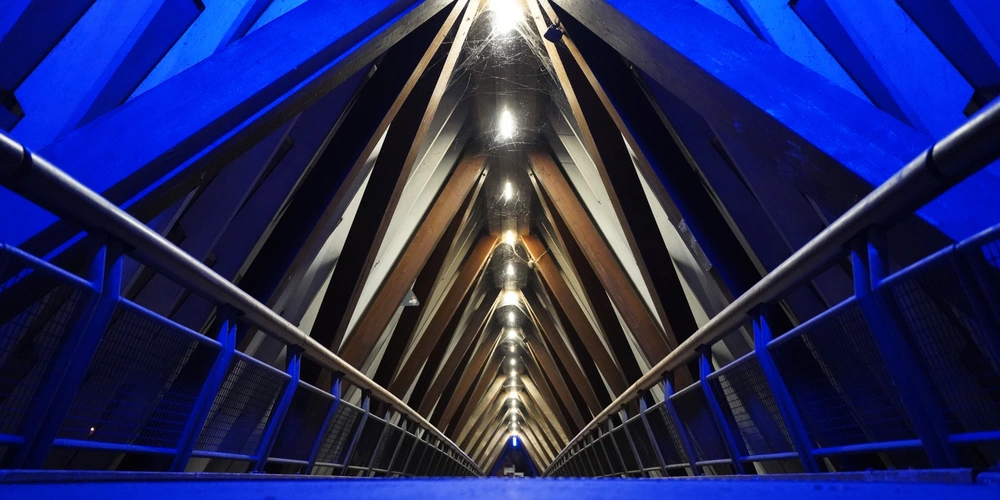 Blick auf einen beleuchteten, blauen Innenraum einer modernen Brücke in symmetrischer Perspektive.