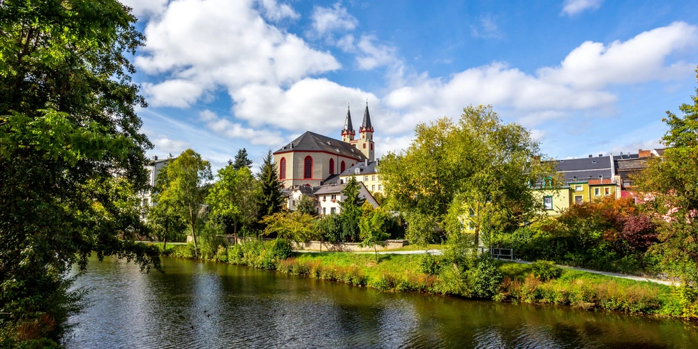Idyllische Landschaft mit einer Kirche und Bäumen am Fluss bei blauem Himmel.