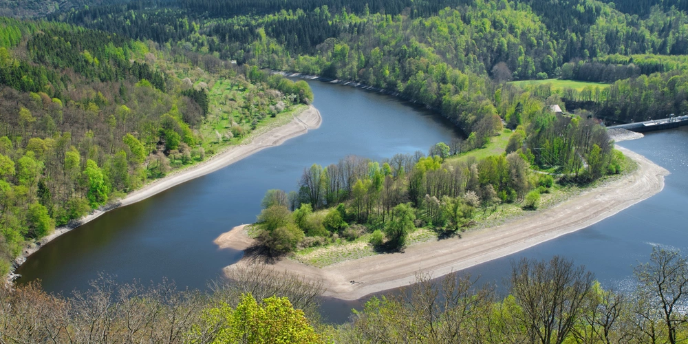 Flusskurve mit grünen Ufern und einem kleinen Sandbank im Sonnenlicht.