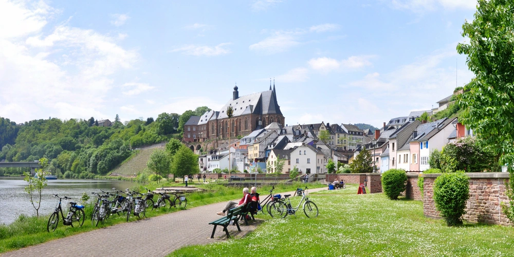 Panorama einer Stadt am Fluss mit Fahrrädern und Häusern unter blauem Himmel.