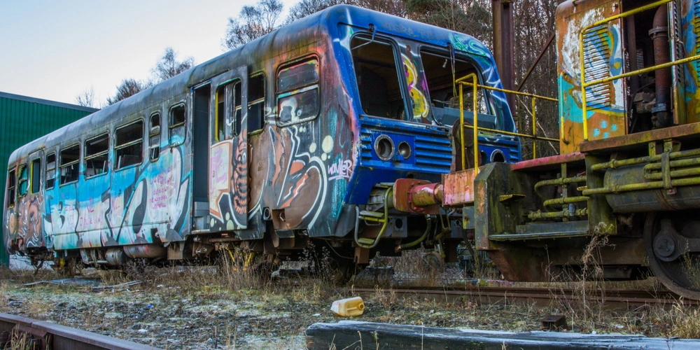 Graffitibedeckter Zugwagen in einer verlassenen Gleislandschaft.