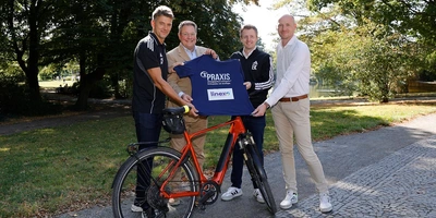 Vertreter von linexo und den Recken halten ein T-Shirt vor einem Fahrrad in einem Park.