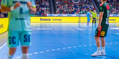 Spieler auf dem Handballfeld, eine Mannschaft in hellblauen, die andere in grünen Trikots.