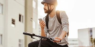 Mann mit Helm sitzt auf einem Fahrrad und schaut auf sein Smartphone