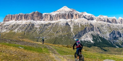 Mountainbiker fahren über eine Wiese in Richtung des Sellastocks der Dolomiten